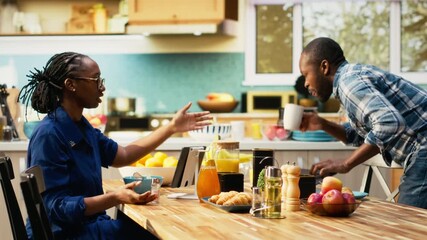 Black woman eating alone after her boyfriend is rushing to leave for work, running late and skipping breakfast. Morning routine in a hurry for man being late for his office job, lifestyle. Camera B.