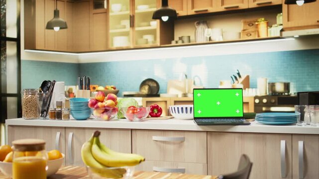 Green screen on laptop in the kitchen with rustic counter and elegant lighting. Cookware and utensils creating a comfortable and inviting household dining space with modern interior design.