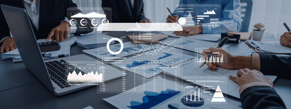 A business team collaborates in a meeting, analyzing graphs and data reports on a laptop and documents, focusing on project development and strategic planning. Trope
