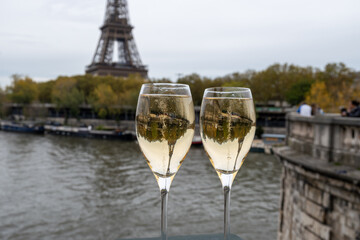 Obraz premium Pouring and drinking of french sparkling wine champagne from tulip glasses with view on Paris streets, buildings, Seine river and towers, wedding event in Paris