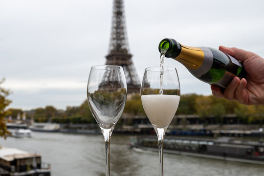 Pouring and drinking of french sparkling wine champagne from tulip glasses with view on Paris streets, buildings, Seine river and towers, wedding event in Paris