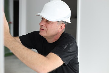 Senior construction electrician working indoors during home renovation, focused professional in safety helmet installing wiring