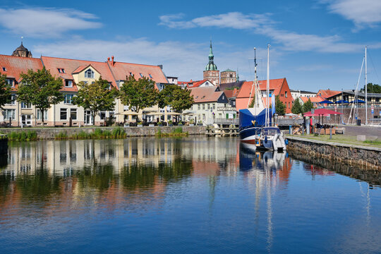 Charming view of Stralsund harbor in Germany with boats, historic buildings, waterfront cafes, and reflections on calm water. Picturesque cityscape ideal for tourism and travel concepts. - Powered by Adobe