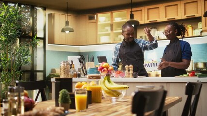 African american man adding pinch of salt to the salad bowl in the kitchen, preparing meal with tasty organic produce. Boyfriend imitating the chef from social media trends, positive energy. Camera A. - Powered by Adobe