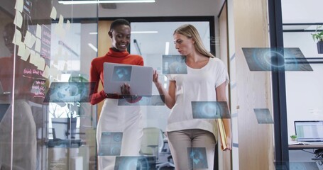 Walking two women in smart attire, holding laptop and files by sticky notes, office AR overlays