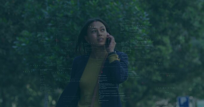 Walking mid-adult woman talking on smartphone along park sidewalk, navy blazer, code overlay