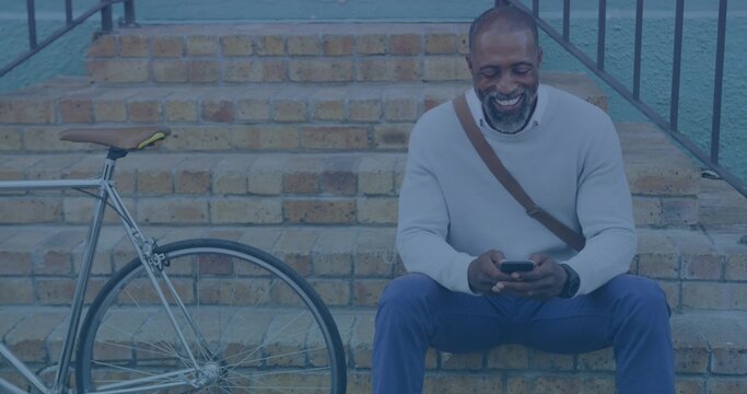 Sitting cyclist in gray sweater checking phone on brick steps, with bicycle, satchel, copy space - Powered by Adobe