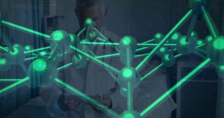 Studying senior doctor in lab coat wearing stethoscope holding tablet in exam room, green hologram