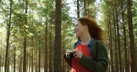 Holding SLR camera with strap, red-haired woman in pine trunks, green jacket red shirt, copy space