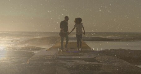 Walking casual couple holding hands along concrete pier at sunset with guitar waves reflecting