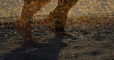 Naklejka premium Walking two adults' bare feet and legs leaving footprints along sandy shore at sunset, golden bokeh