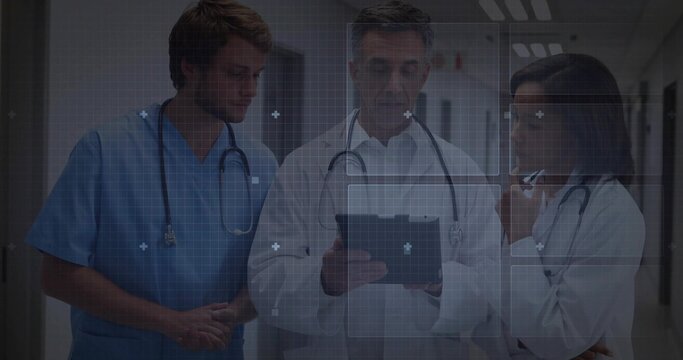 Reviewing tablet staff in lab coats, blue scrubs consulting in hospital corridor with stethoscopes