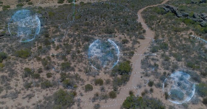 Hovering aerial arid scrubland revealing three blue holographic spheres over winding dirt trail