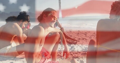 Smiling shirtless man wearing red trunks chatting with friends on sandy beach, flag overlay