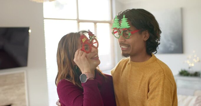 Diverse couple hugging, straightening glasses, wearing smartwatch, pressing cheek, laughing at home