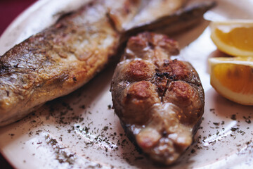 Montenegrin cuisine, fish assortment platter, fried grilled crucian carp steak, roasted pastrmka and bleak on plate with lemon and salad served in a restaurant in Montenegro, Skadar lake, Virpazar