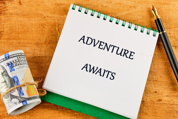 On a rustic wooden table, a notepad features the phrase adventure awaits, paired with a rolled bill and an elegant pen, inspiring thoughts of travel and exploration