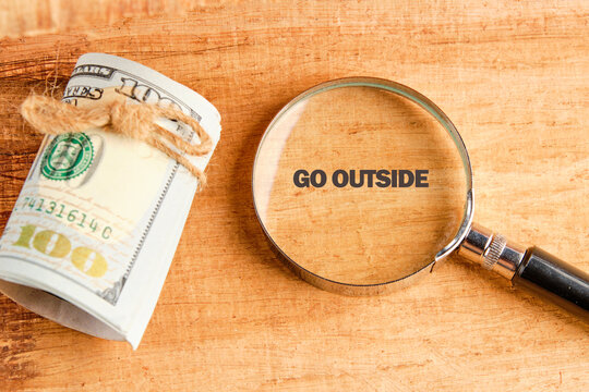 A rolled bundle of money rests beside a magnifying glass highlighting the words go outside