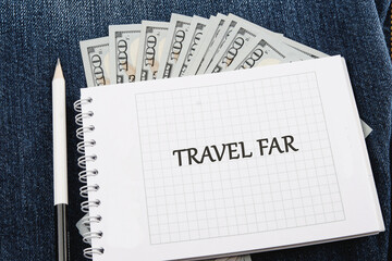 A travel note book titled Travel Far sits on denim fabric alongside a stack of cash, symbolizing dreams of exploration and adventure in distant lands ahead