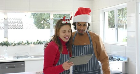 Diverse couple scrolling recipes on tablet at kitchen while holiday planning and leaning laughing - Powered by Adobe
