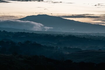 Dawn breaks over a mountainous landscape with mist rising and clouds drifting in the early morning light