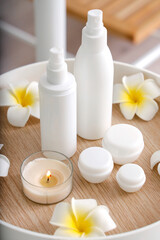 Cosmetic products with burning candle and plumeria flowers on tray in spa salon, closeup