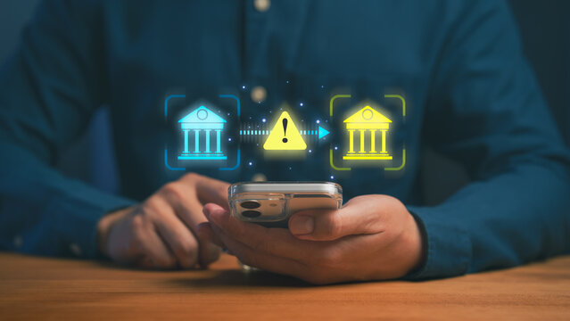 Person using a smartphone with digital bank icons and a warning symbol, illustrating online banking risks, payment transfer issues, security alerts, scammer, and financial transaction protection.
