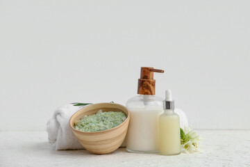 Bowl of sea salt, cosmetic products and clean towel on light background