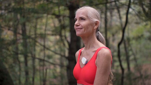 Woman with silver hair wearing a heart monitor in a natural environment while smiling, showing her commitment to health and wellness