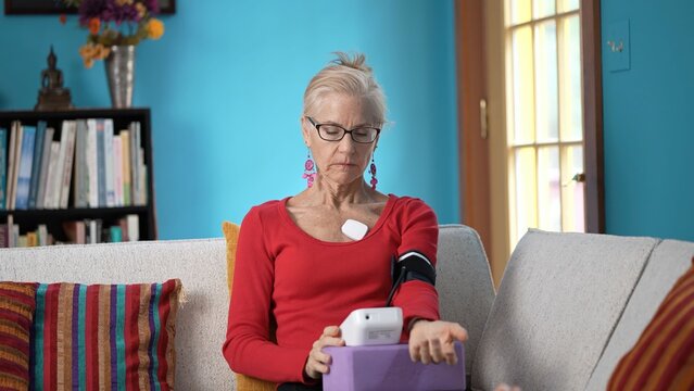 Mature woman smiles while using a heart monitor to track atrial fibrillation at home, focusing on her health and wellness - Powered by Adobe