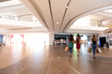 Obraz premium Blurred shoppers stroll through modern mall, carrying bags. Bright lights and sleek architecture create vibrant, bustling retail atmosphere.