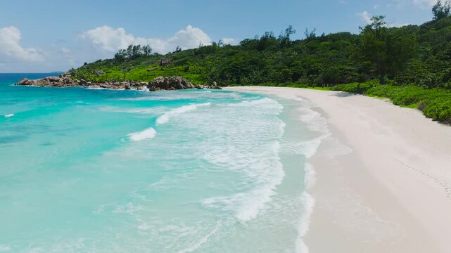 Aerial view of a tropical coastline featuring a white sand beach and clear turquoise waters. Anse Cocos beach. La Digue, Seychelles.