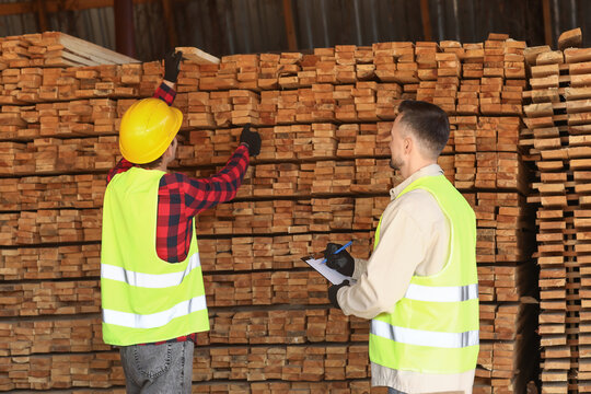 Male carpenters working near wooden planks at sawmill - Powered by Adobe