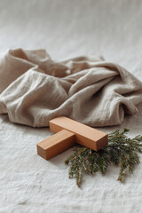 wooden cross lies gently on linen tablecloth accompanied by sprig of fir