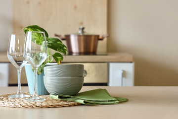 Clean dishes with green napkin and plant on table in kitchen, closeup