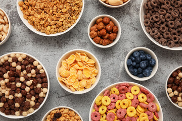 Bowls with different tasty cereals, berries and nuts on grunge grey background