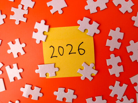 Yellow sticky note with the number 2026 surrounded by white jigsaw puzzle pieces on an orange background