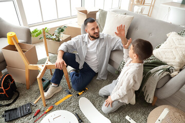 Father with his son giving each other high-five while assembling chair at home