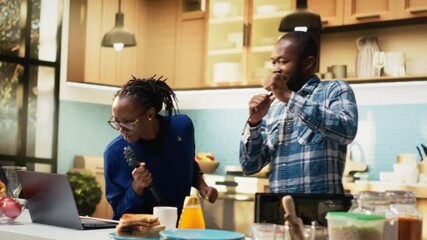 Energetic man and woman singing and laughing in the kitchen, enjoying relaxed morning at home with music. Fun romantic activity shows love, satisfaction and modern lifestyle full of joy. Camera B.