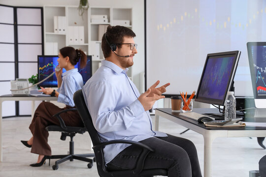 Male trader with headset working at table in office - Powered by Adobe