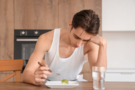 Young man with anorexia eating broccoli in kitchen