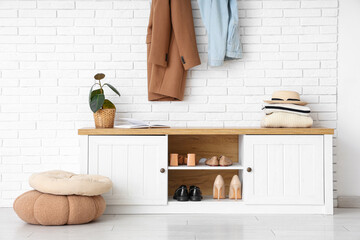 Poufs and bench with shoes near white brick wall in hallway, closeup