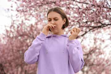 Allergic young woman with tissue sneezing in park