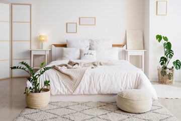 Interior of light bedroom with comfortable bed, bedside table and houseplants
