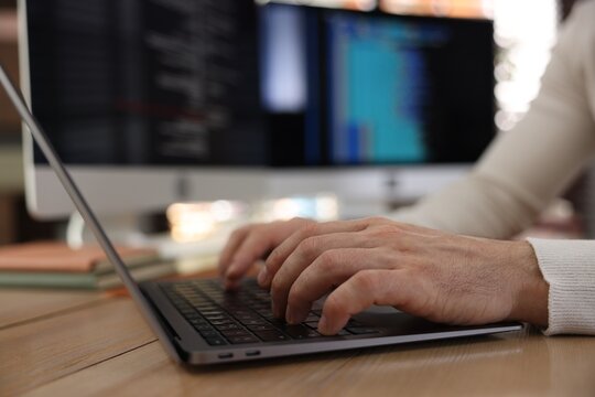 Programmer working on laptop at wooden table indoors, closeup