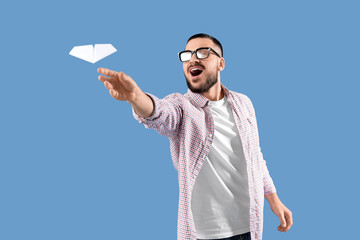 Young man throwing paper plane on blue background