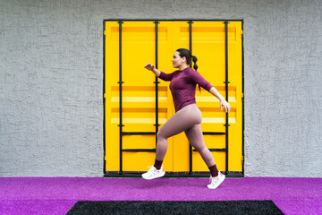 Active hispanic woman engaging in a fitness workout, doing a lunge against a vibrant yellow and grey urban background