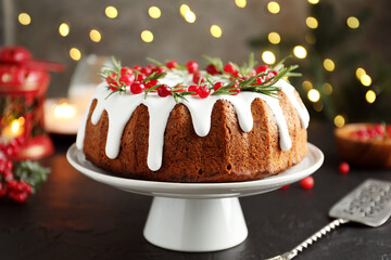 Tasty Christmas cake with icing, cranberries and rosemary on black table against blurred lights, closeup
