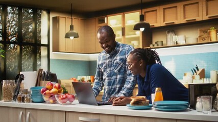 Cheerful lovers preparing delicious breakfast meal and drinking coffee together, following online steps from laptop. Serving toast slices and homemade croissants, healthy food. Camera A. - Powered by Adobe