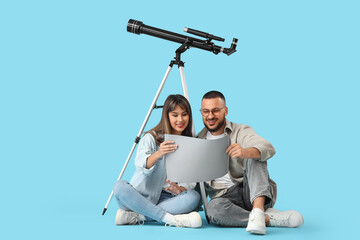 Young couple with map and telescope sitting on blue background